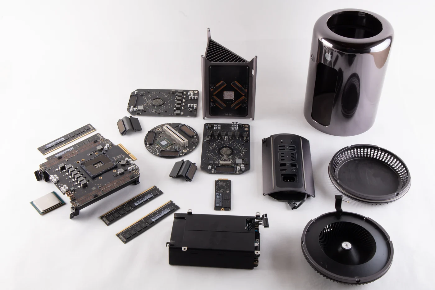 A 2013 Mac Pro fully torn down — cylinder case, logic boards, RAM modules, SSD, fans, and housing laid out in an organized grid.